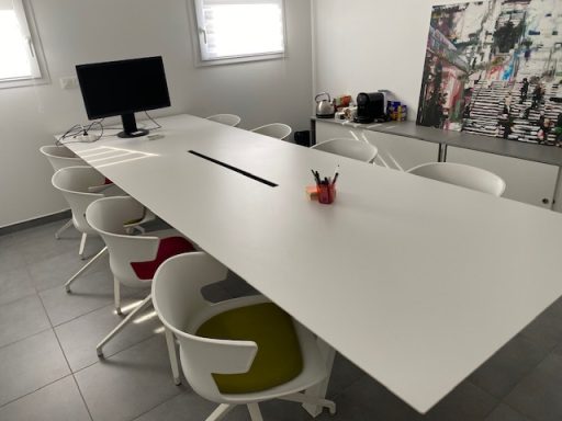 Salle de réunion moderne avec table blanche, chaises colorées et ordinateur.