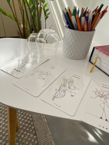 Trois cartes illustrées sur une table avec un pot de stylos et un livre en arrière-plan.