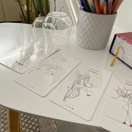 Cartes illustrées sur une table, accompagnées de stylos et d'objets de décoration.